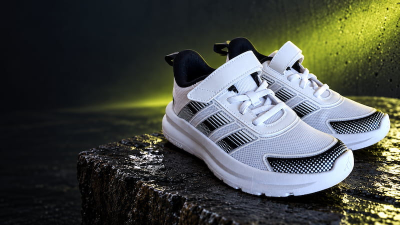 Paire de chaussures blanches et noires sur un socle minéral sombre, avec un éclairage vert citron et un espace libre à gauche pour le texte.